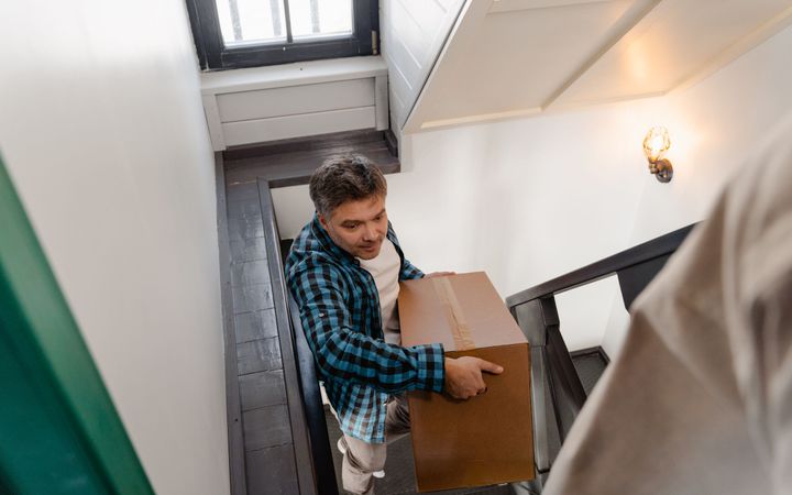 Umzugshelfer tragen einen verpackten Schrank durch ein Treppenhaus