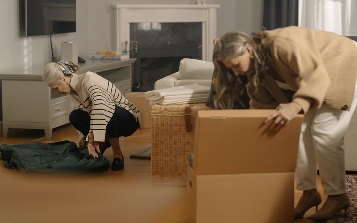 Umzugshelfer unterstützt eine ältere Person beim Einpacken von Geschirr